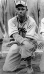 A baseball player sitting on the ground in front of other players.