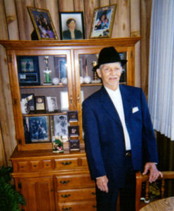 A man in a suit and hat standing next to a wooden cabinet.